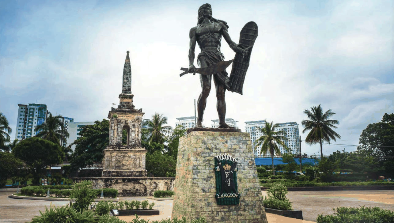 Lapu-Lapu statue holding a shield and kampilan beside the Magellan Shrine obelisk in Mactan