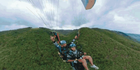 Tandem paragliders flying over green hills in Oslob